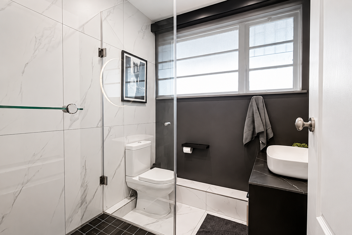 Modern bathroom featuring marble-look wall tiles, a glass shower screen, a vessel sink vanity, and a toilet with dark floor tiling.