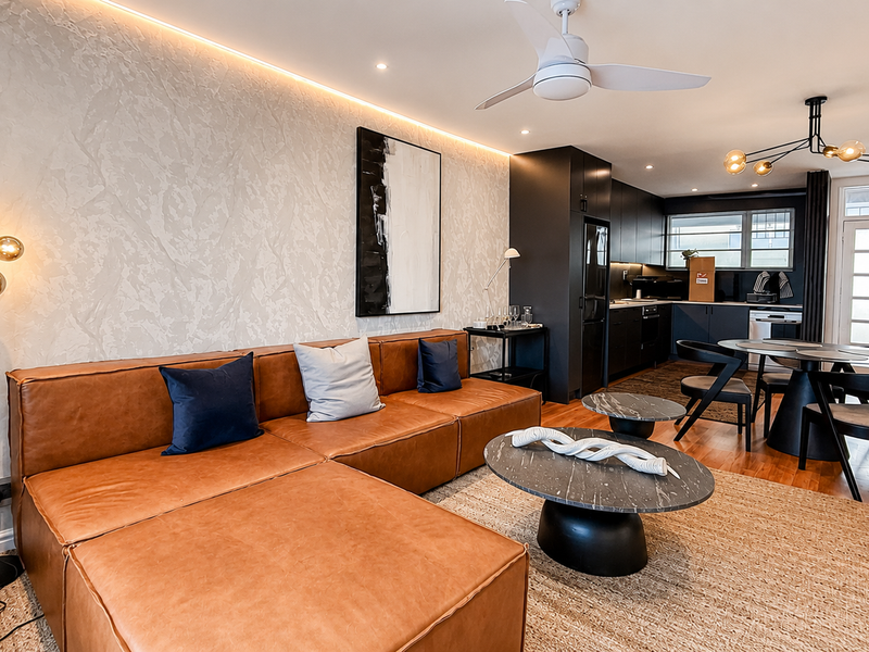 Modern open-plan living and kitchen area featuring a textured feature wall with ambient LED lighting, hardwood floors, and contemporary built-in cabinetry.