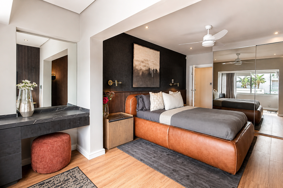 A modern, well-appointed bedroom featuring timber laminate flooring, a sleek built-in vanity, mirrored wardrobes, and stylish slatted wall paneling with integrated lighting.