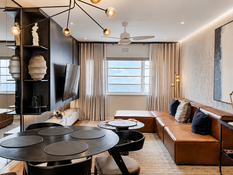 Modern living room featuring a textured feature wall, built-in shelving, mirrored wall accents, and a ceiling fan, creating a sophisticated and well-maintained space.