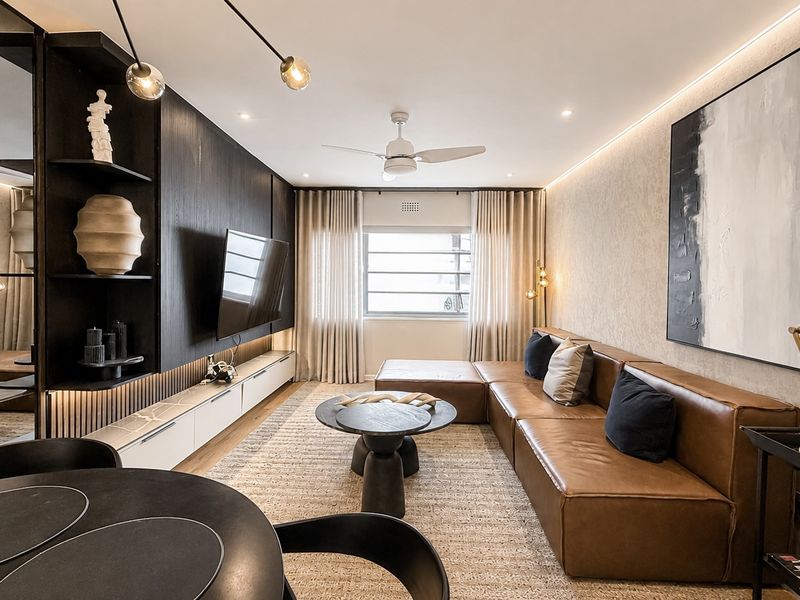 Modern, well-appointed living room featuring custom built-in cabinetry, integrated LED lighting, a ceiling fan, and a sophisticated mirrored feature wall.