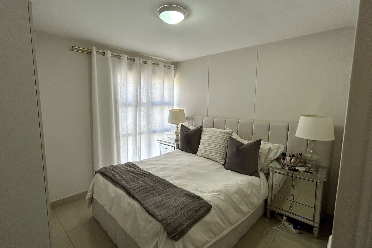 A well-maintained bedroom featuring neutral tiled flooring and a ceiling-mounted light fixture, providing a clean and comfortable living space.