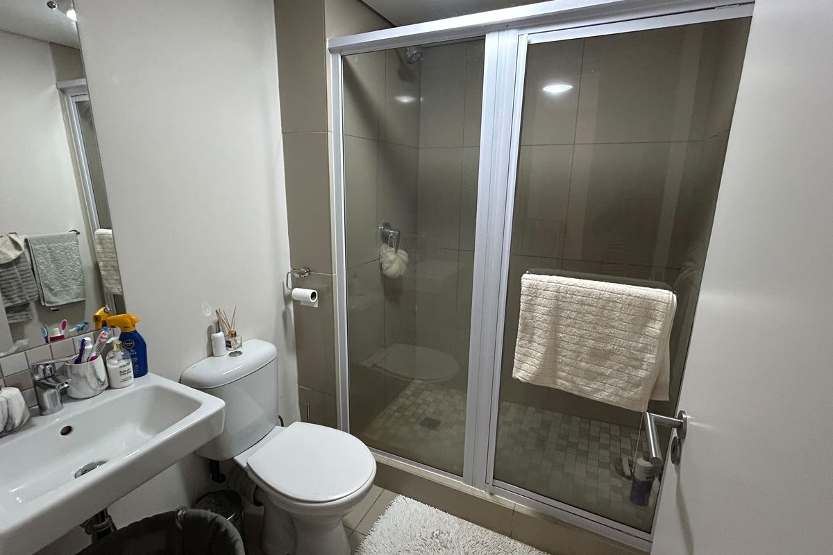 A functional bathroom featuring a glass-enclosed shower, wall-mounted basin, and standard toilet with neutral wall tiling.