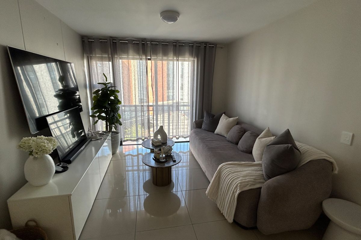 A well-lit living room featuring polished tiled flooring and a large sliding glass door providing access to the balcony.