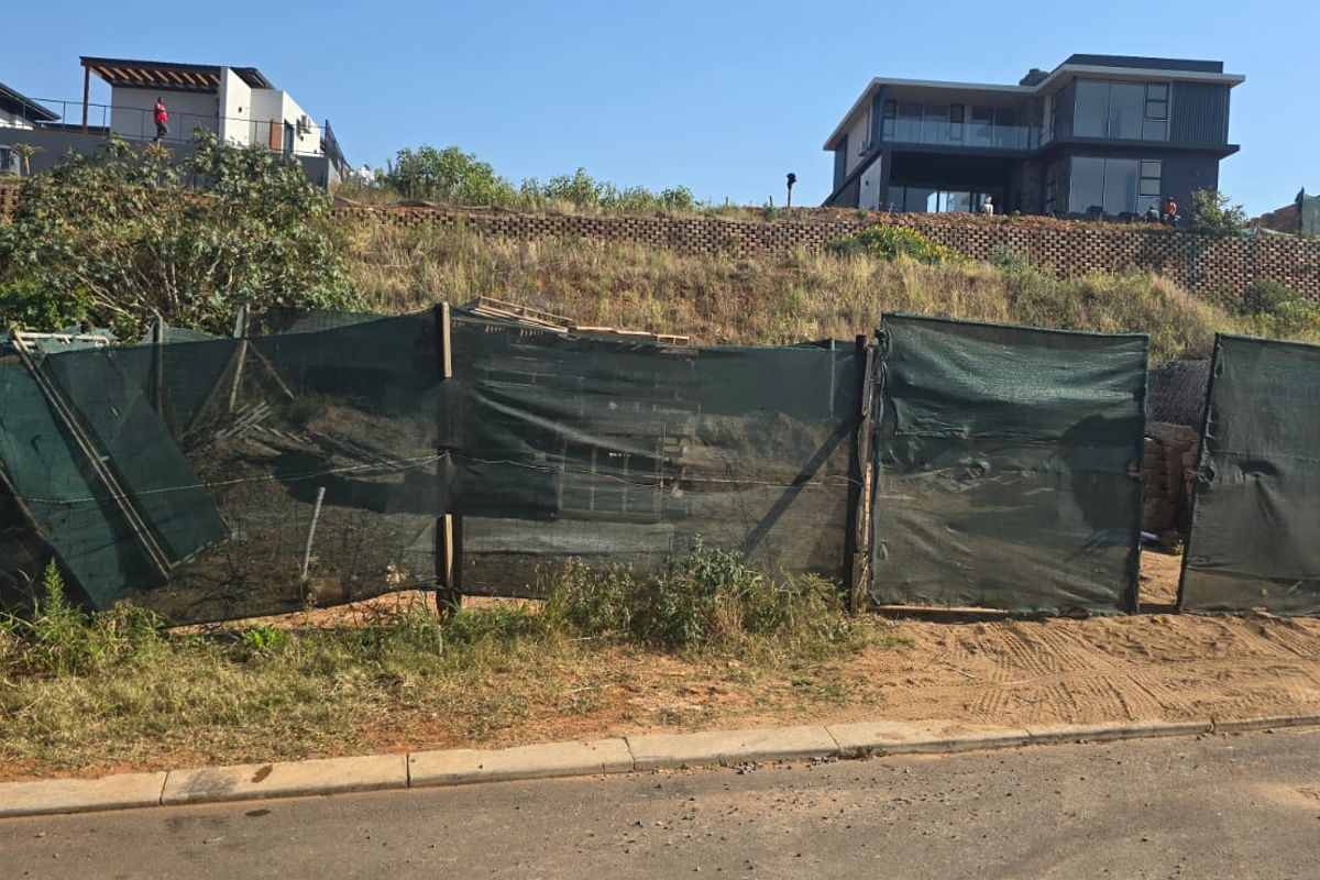 A vacant residential plot featuring a sloped terrain with a retaining wall, currently enclosed by temporary construction netting.
