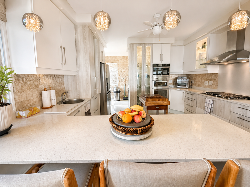 Modern kitchen featuring stone benchtops, integrated stainless steel appliances, gas cooktop, and stylish pendant lighting with a neutral color palette.
