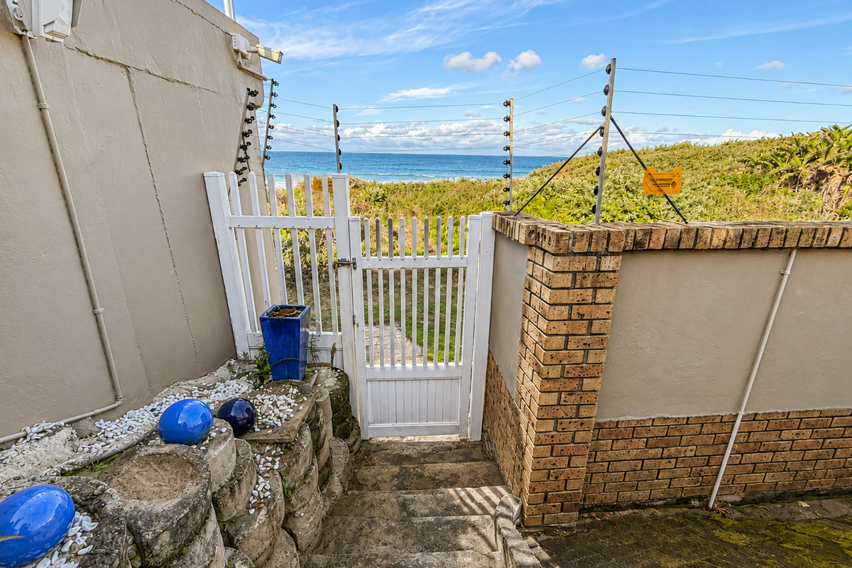 Rear access gate featuring electric fencing, brick boundary wall, and stone retaining wall, leading towards a coastal view.
