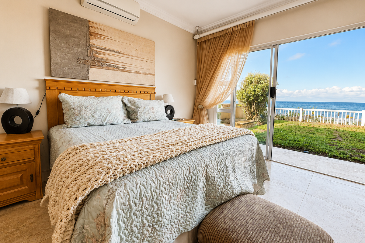 Spacious bedroom featuring tiled flooring, crown molding, and a split-system air conditioner, with direct access to a patio and ocean views through sliding doors.