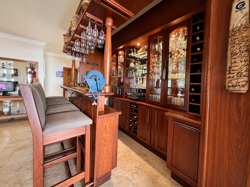 A well-appointed home bar featuring custom wooden cabinetry, integrated wine storage, glass display shelving, and a dedicated bar counter with overhead glassware storage.
