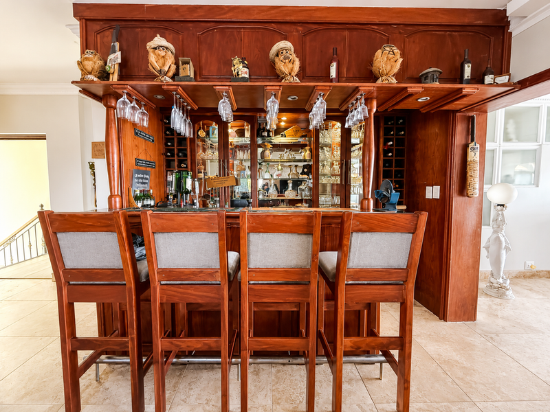 A dedicated home bar area featuring custom built-in wooden cabinetry, integrated wine storage, glass shelving, and recessed lighting.