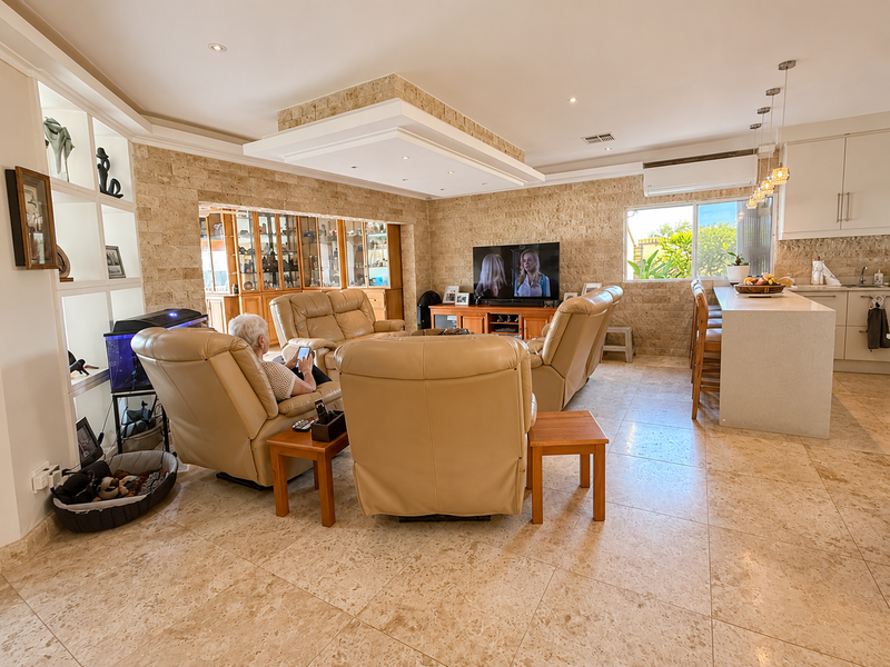 Spacious open-plan living area featuring elegant travertine stone wall cladding, a modern kitchen island, and a sophisticated recessed ceiling design with integrated lighting.