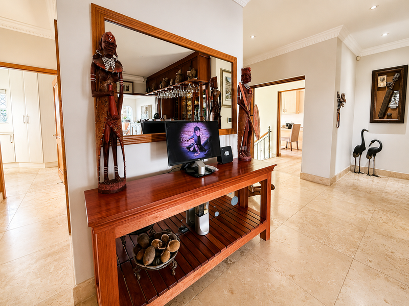 Spacious hallway featuring polished tile flooring, crown molding, recessed lighting, and a built-in bar area with mirror and glass storage.