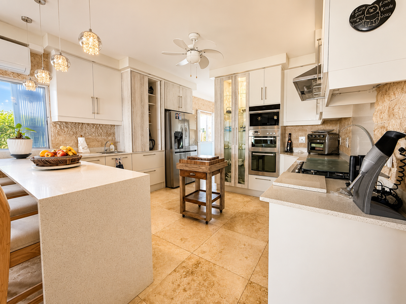 Modern kitchen featuring high-end quartz countertops, built-in double ovens, stone tile flooring, and elegant textured stone backsplash with ample cabinetry.
