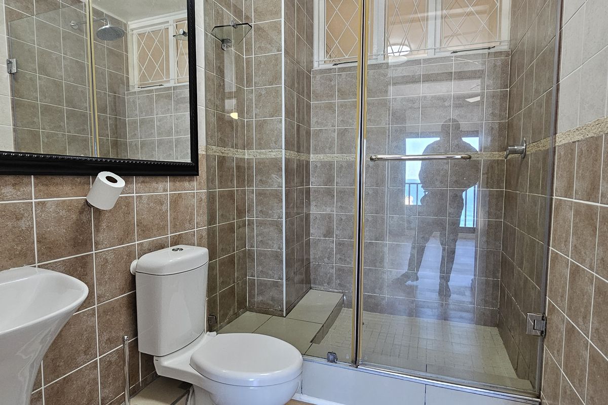 A functional bathroom featuring a glass-enclosed shower, wall-mounted basin, and toilet, finished with neutral-toned wall and floor tiles.
