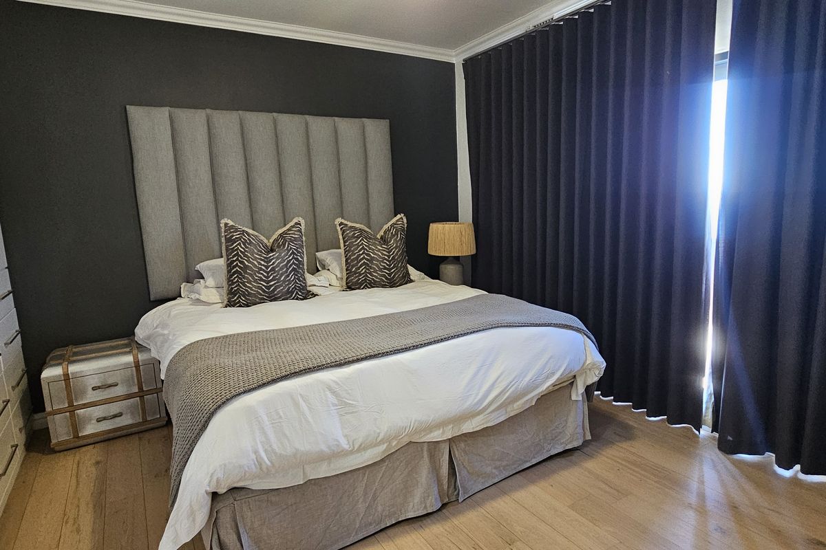 A well-maintained bedroom featuring timber flooring, built-in wardrobes, and floor-to-ceiling curtains leading to an outdoor area.
