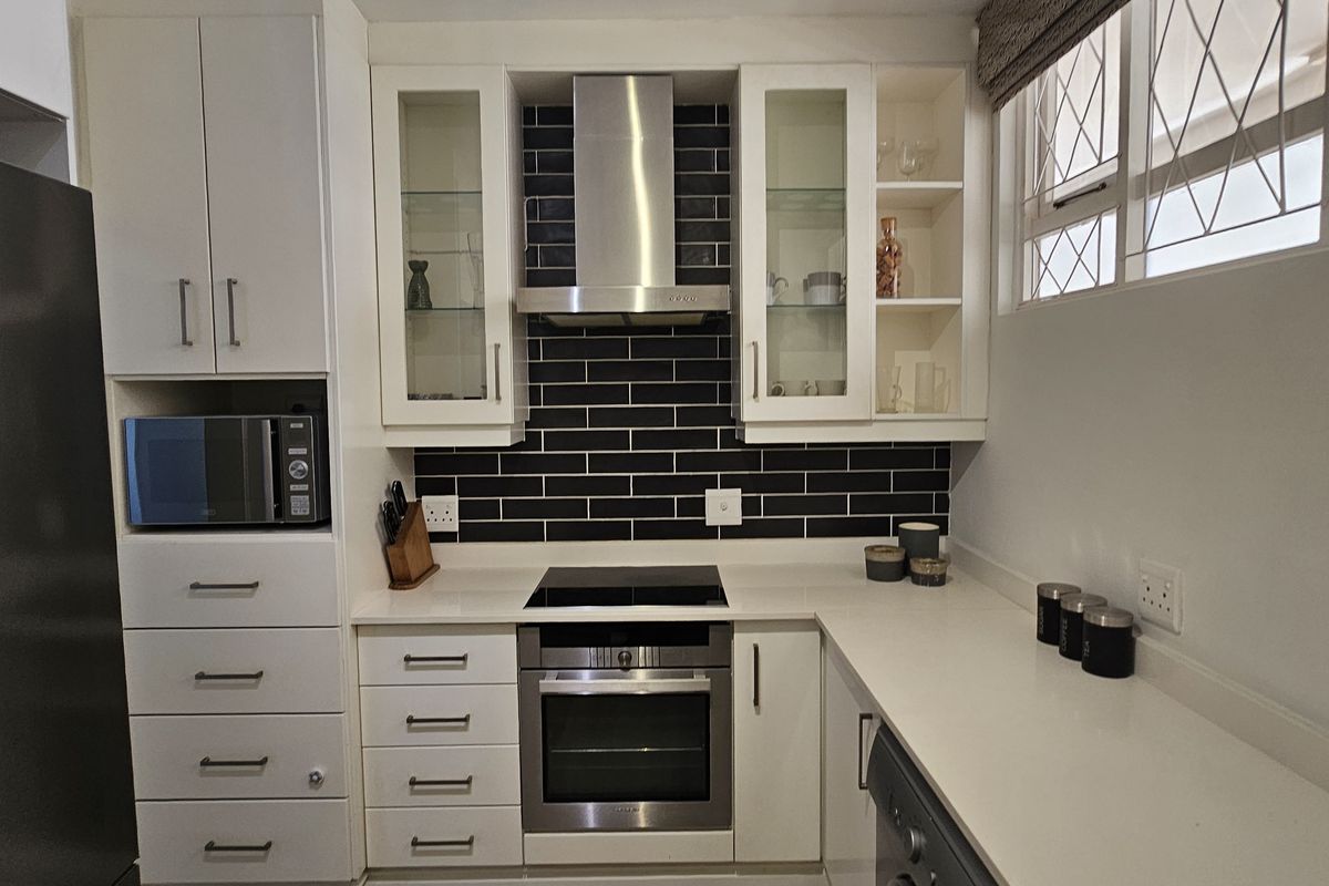 Modern kitchen featuring white cabinetry, quartz countertops, a dark subway tile backsplash, and integrated stainless steel appliances.