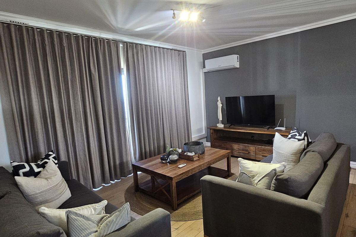 A well-maintained living room featuring hardwood flooring, crown molding, and a wall-mounted air conditioning unit, complemented by floor-to-ceiling curtains.