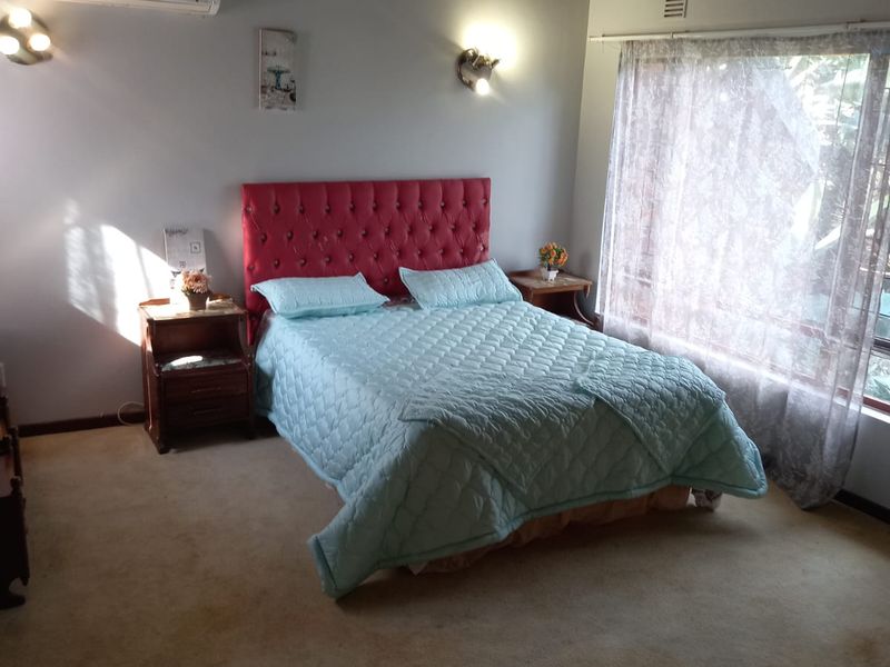 Spacious bedroom featuring a vaulted timber ceiling, wall-mounted air conditioning, and large windows allowing natural light.
