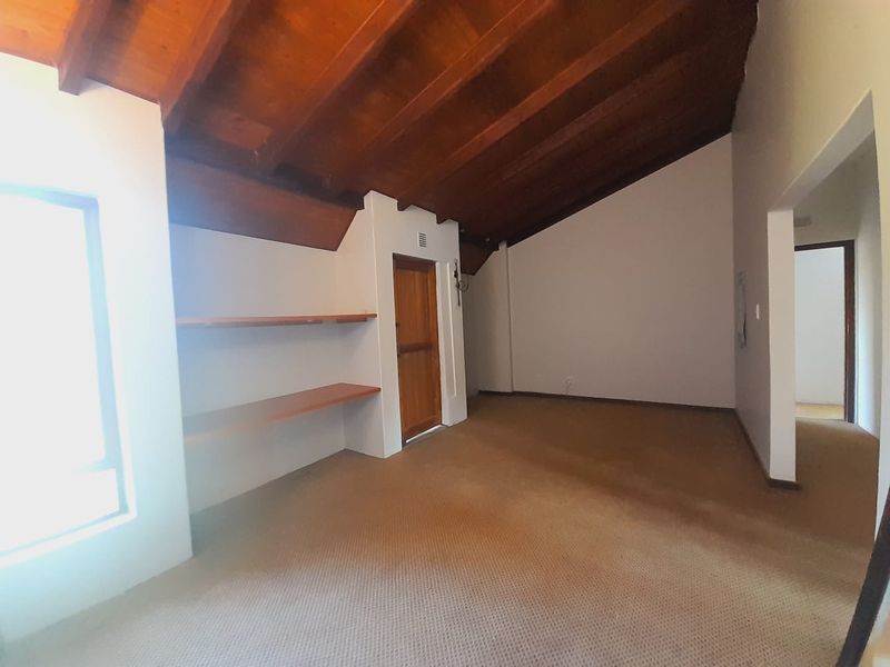 Spacious bedroom featuring a high exposed timber raked ceiling, built-in shelving, and neutral carpeted flooring.