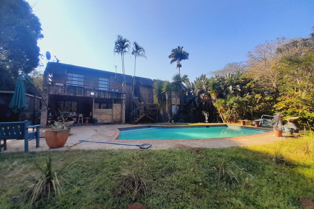 Rear view of the property featuring a swimming pool, paved deck area, and a two-story building facade with a balcony and external staircase.