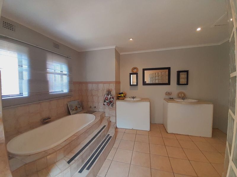Spacious bathroom featuring a raised built-in bathtub, dual vanity basins, and neutral tiled finishes, offering a functional layout with potential for modern updates.