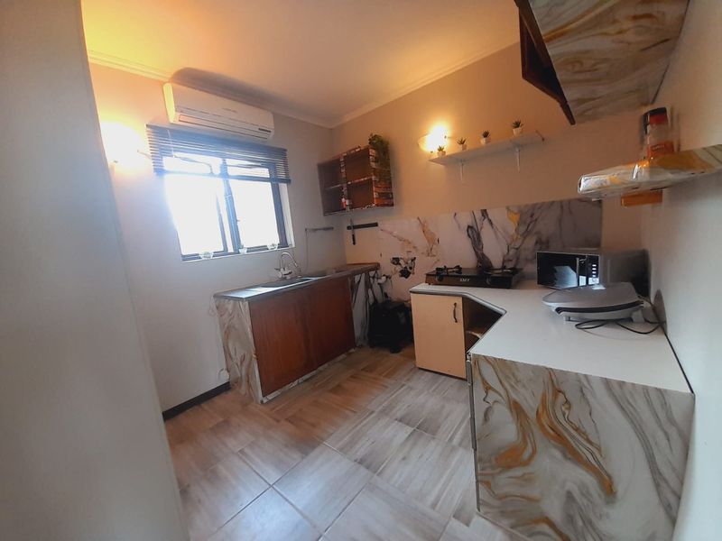 A functional kitchen featuring marble-effect countertops, built-in cabinetry, a gas hob, and a wall-mounted air conditioning unit.
