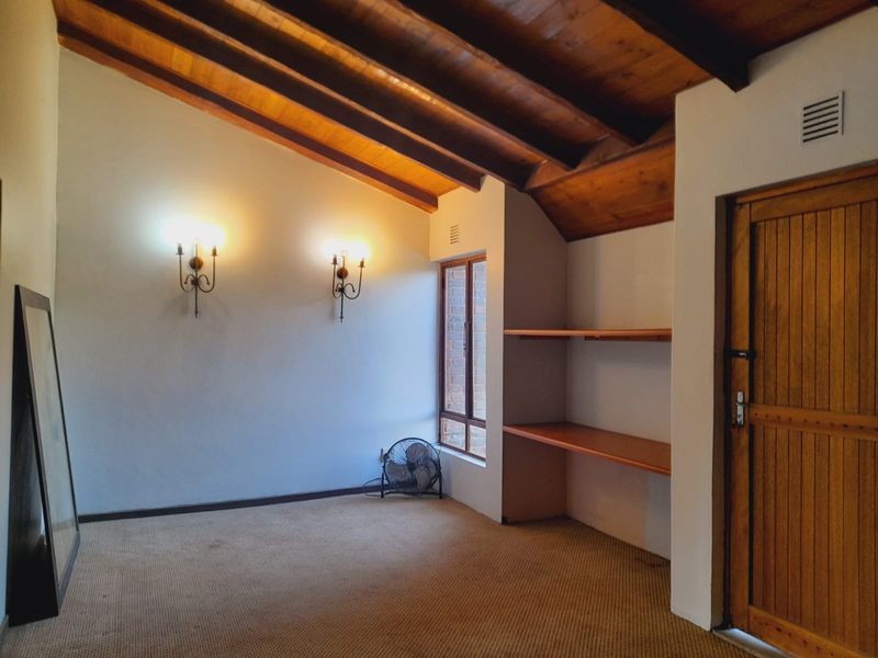 A bedroom featuring a vaulted timber ceiling, built-in shelving, and wall-mounted lighting, offering a cozy atmosphere with potential for modern updates.