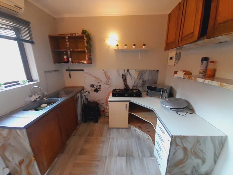 Compact kitchen featuring wooden cabinetry, a double basin sink, gas hob, and marble-effect splashback, requiring some maintenance to the cabinetry.