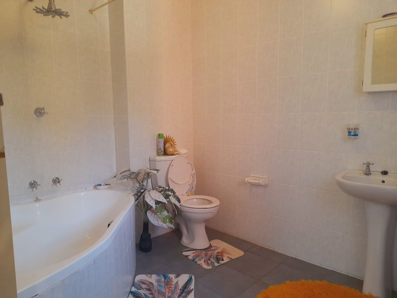 A functional bathroom featuring a corner bathtub with shower, pedestal sink, and toilet, finished with neutral wall tiles and grey floor tiles.