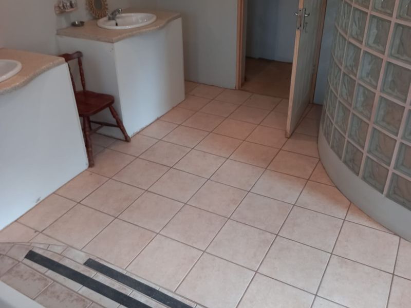 Bathroom featuring a dual vanity, a curved glass block shower enclosure, and a built-in bathtub with tiled steps.