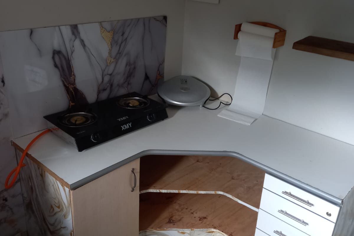A compact kitchen corner featuring a gas hob, marble-effect splashback, and white cabinetry with an open storage section.