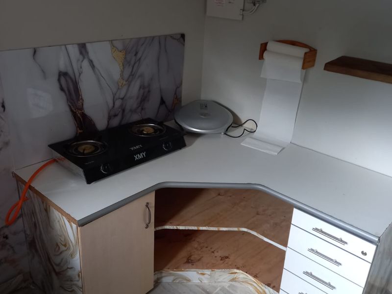 A compact kitchen corner featuring a gas hob, marble-effect splashback, and white cabinetry with an open storage section.
