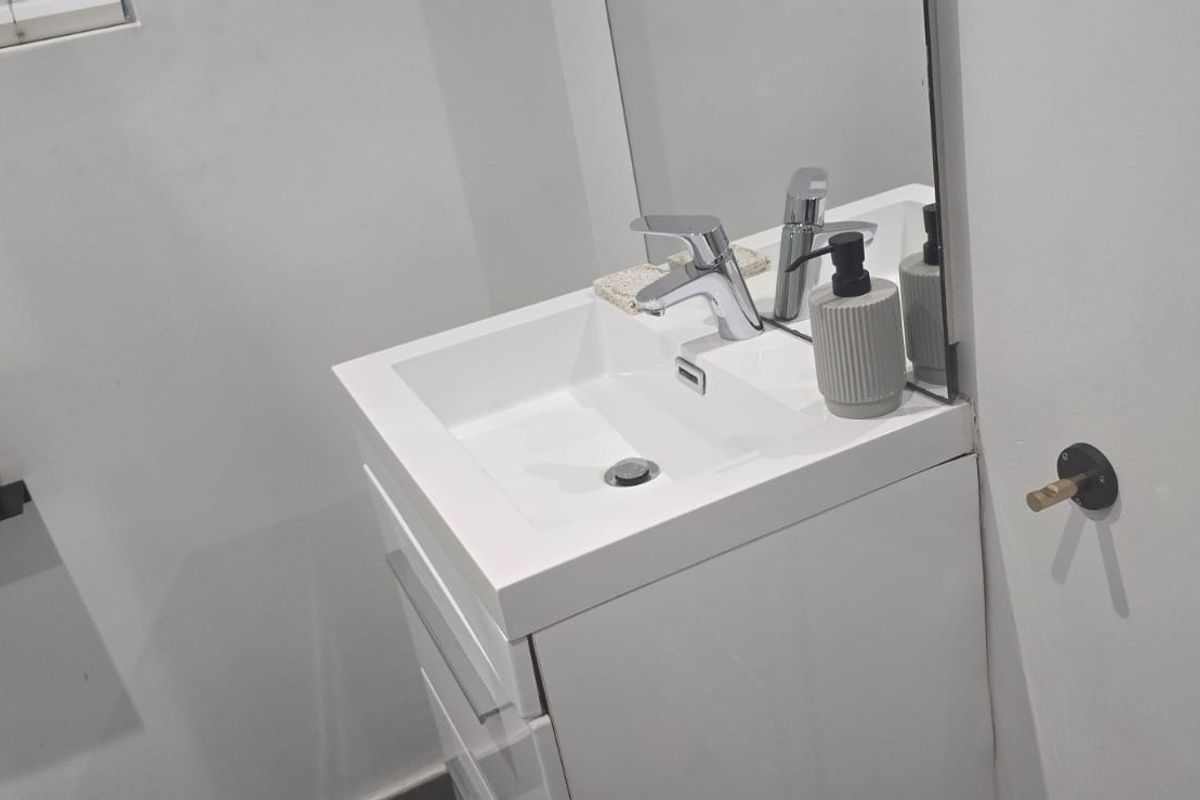 A modern bathroom featuring a sleek white vanity cabinet with a basin, chrome mixer tap, and a wall-mounted mirror.