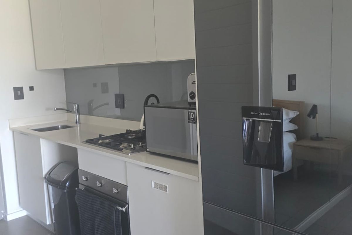A modern, compact kitchen featuring sleek white cabinetry, a gas hob, built-in oven, and a glass splashback with stone countertops.