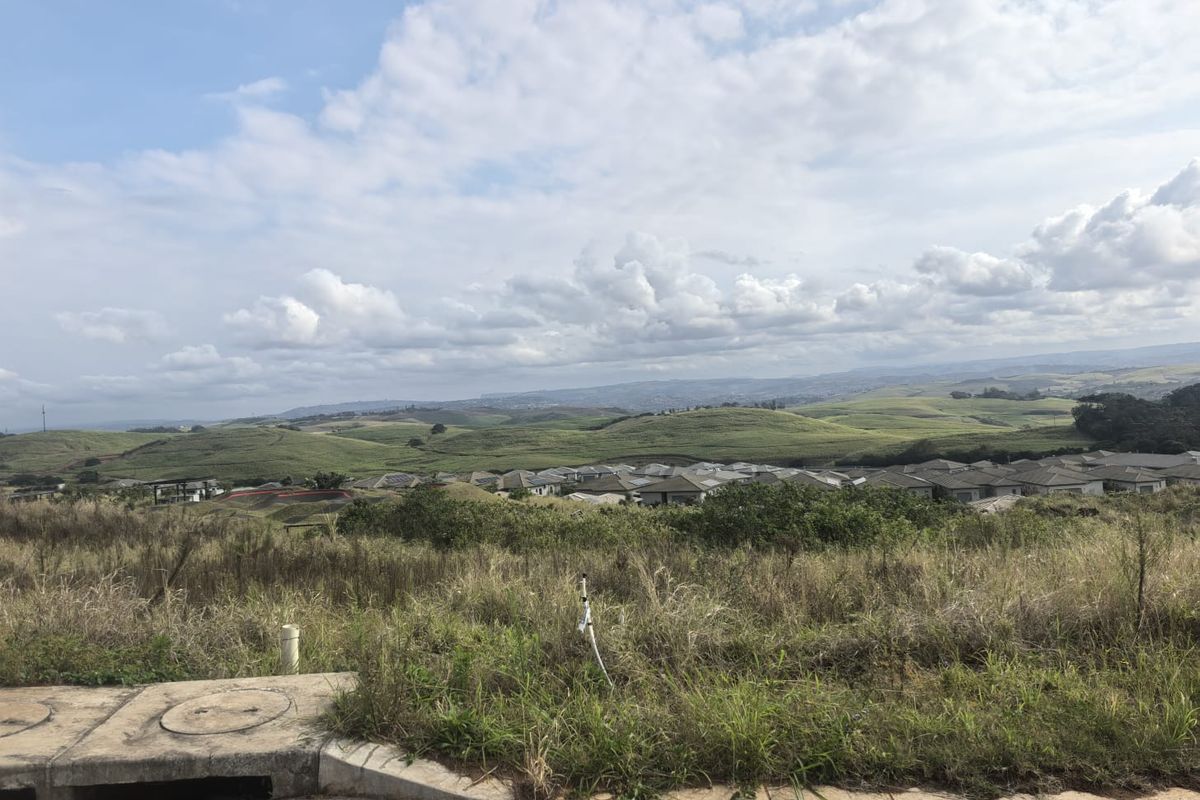 A scenic view overlooking rolling green hills and a residential estate from a vacant residential plot.