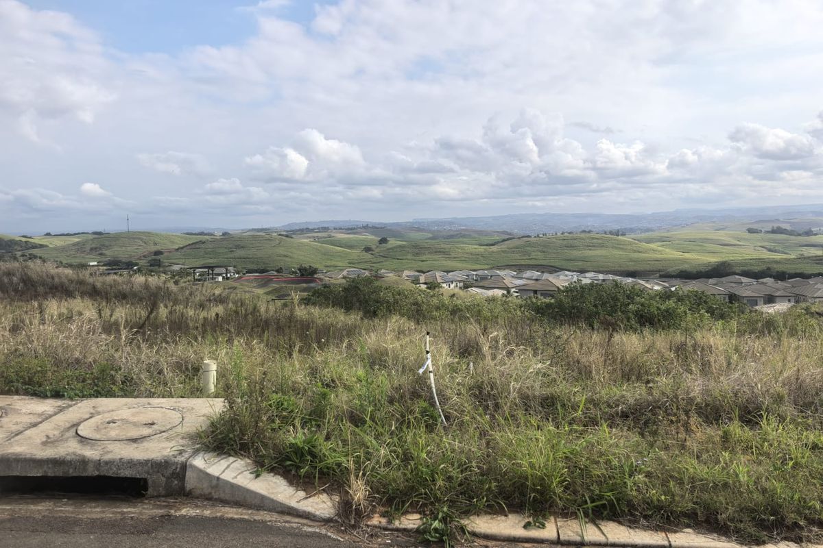 A view of the surrounding landscape and residential area from the vacant residential plot, featuring natural vegetation and established infrastructure.