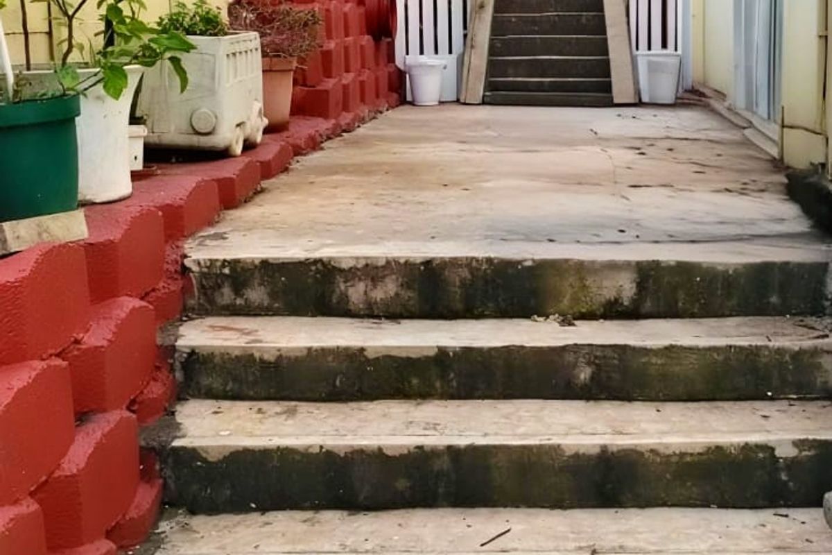 Rear exterior area featuring concrete stairs, a painted retaining wall, and a white picket fence leading to an elevated section of the property.