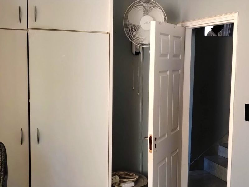 A bedroom interior featuring built-in cupboards and a wall-mounted fan, providing functional storage and ventilation.