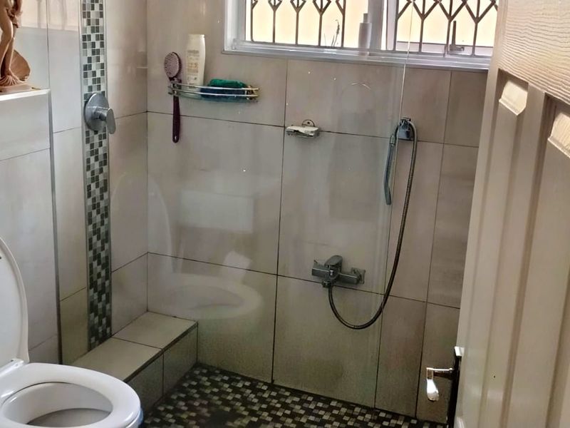 A functional bathroom featuring a wall-mounted toilet with a concealed cistern and a tiled shower area with a handheld shower fixture.