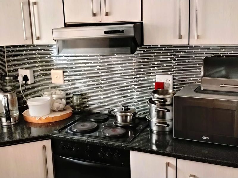 A functional kitchen featuring dark granite countertops, light-toned cabinetry, a modern electric hob with extractor fan, and a decorative mosaic tile backsplash.