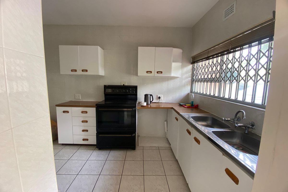 A functional kitchen featuring white cabinetry, a double bowl stainless steel sink, tiled flooring, and a freestanding stove with a security-fitted window.