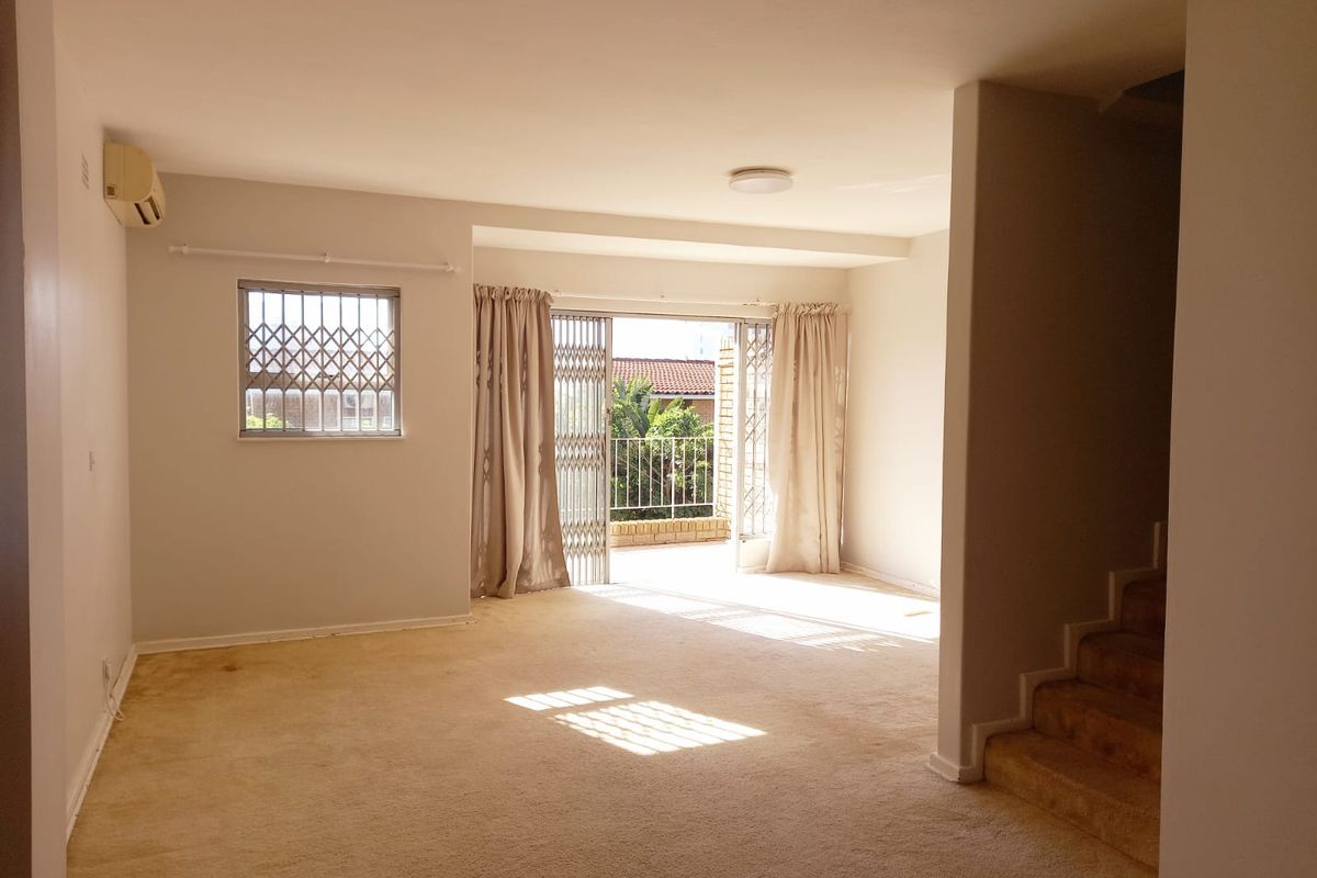 Spacious, empty living area featuring carpeted flooring, a wall-mounted air conditioner, and a sliding door leading to an outdoor balcony.