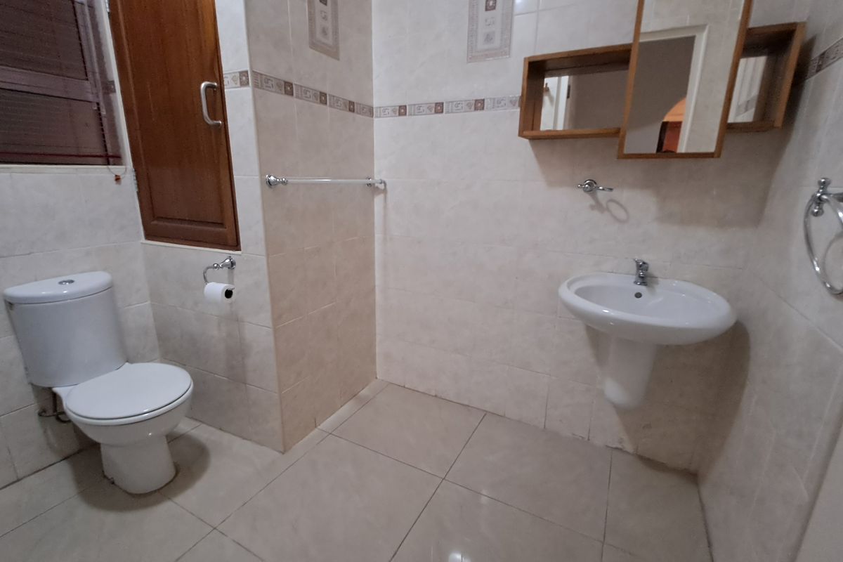 A functional bathroom featuring a pedestal basin, toilet, and neutral wall and floor tiling, offering a clean and practical space.