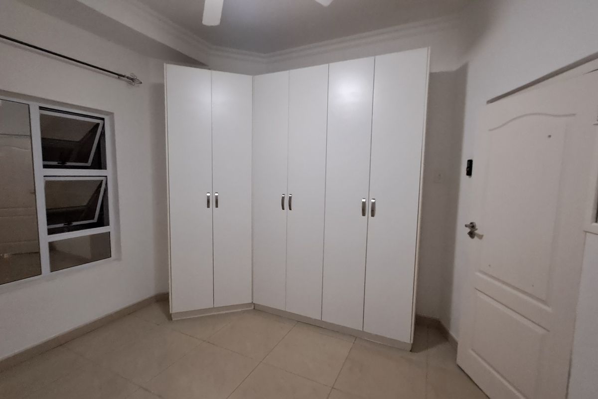 A clean, empty bedroom featuring neutral tiled flooring, white built-in cupboards, and a ceiling fan, offering a blank canvas for personalization.