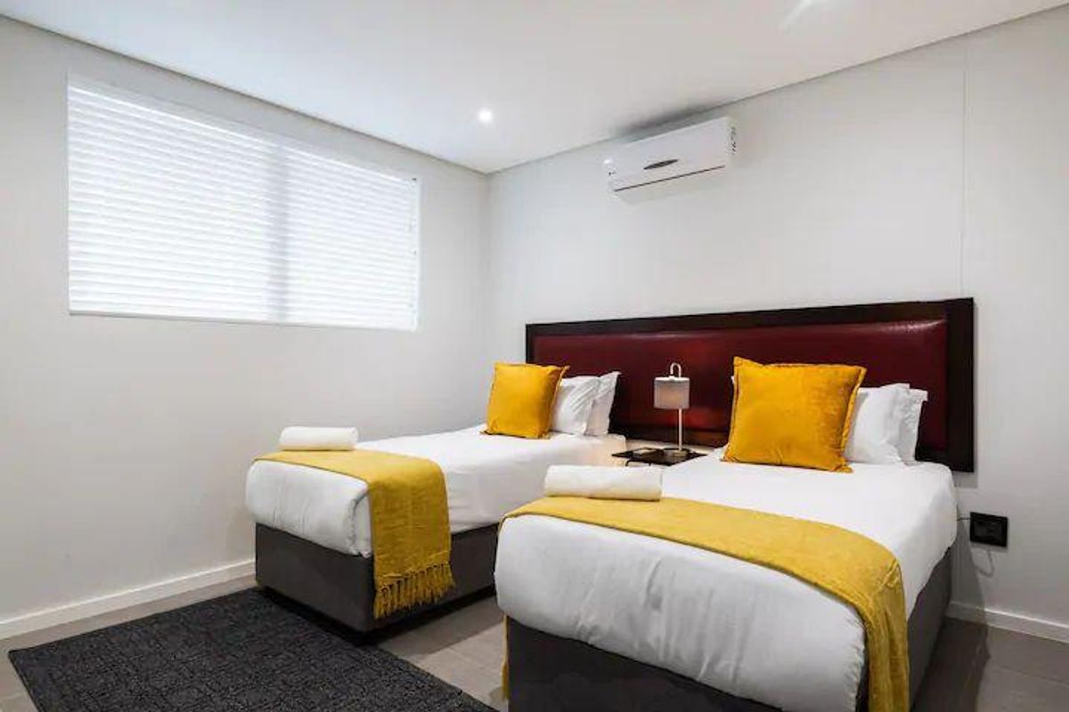 A well-maintained bedroom featuring tiled flooring, recessed downlighting, a wall-mounted split-system air conditioner, and venetian blinds.