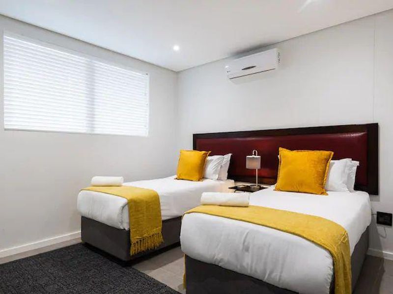 A well-maintained bedroom featuring tiled flooring, recessed downlighting, a wall-mounted split-system air conditioner, and venetian blinds.