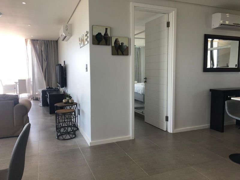 Open-plan living area featuring neutral tiled flooring, recessed lighting, and split-system air conditioning, with direct access to an adjoining bedroom.