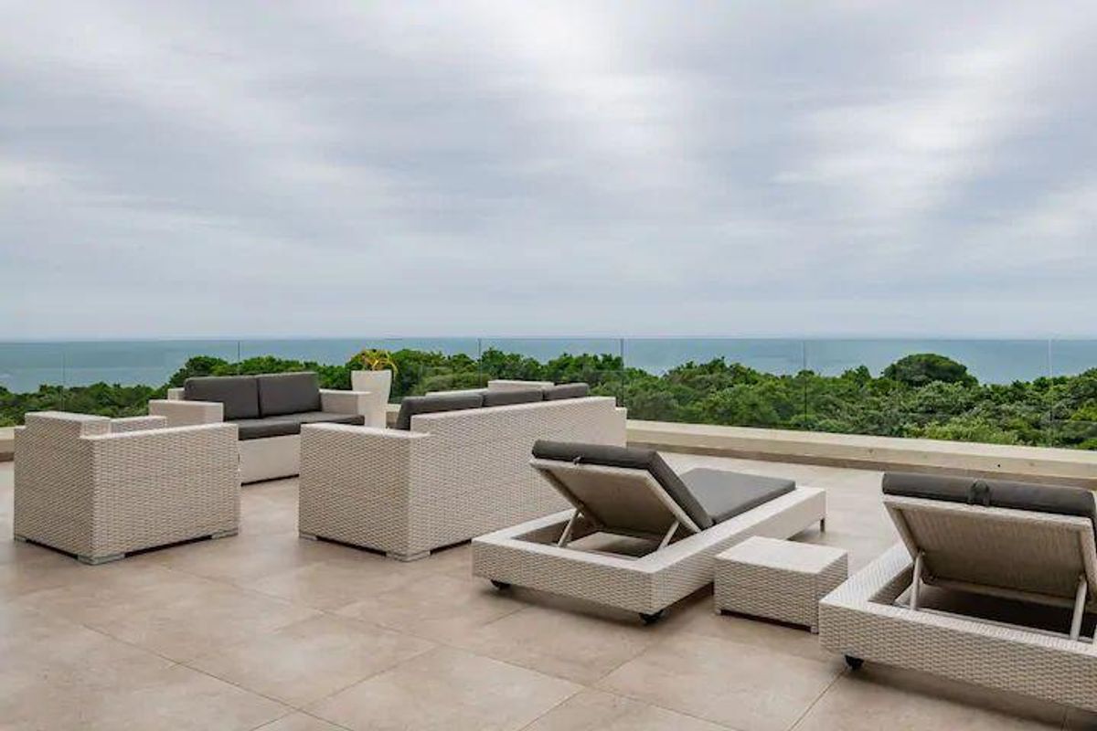 Spacious outdoor balcony featuring modern tiled flooring and a frameless glass balustrade, offering expansive ocean and forest views.