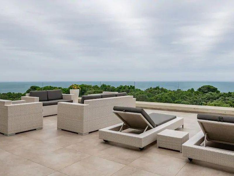 Spacious outdoor balcony featuring modern tiled flooring and a frameless glass balustrade, offering expansive ocean and forest views.