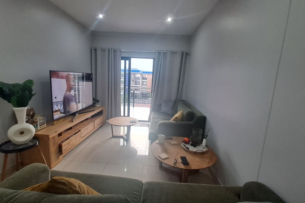 A well-lit living room featuring tiled flooring, recessed downlighting, and direct access to a balcony through sliding glass doors.
